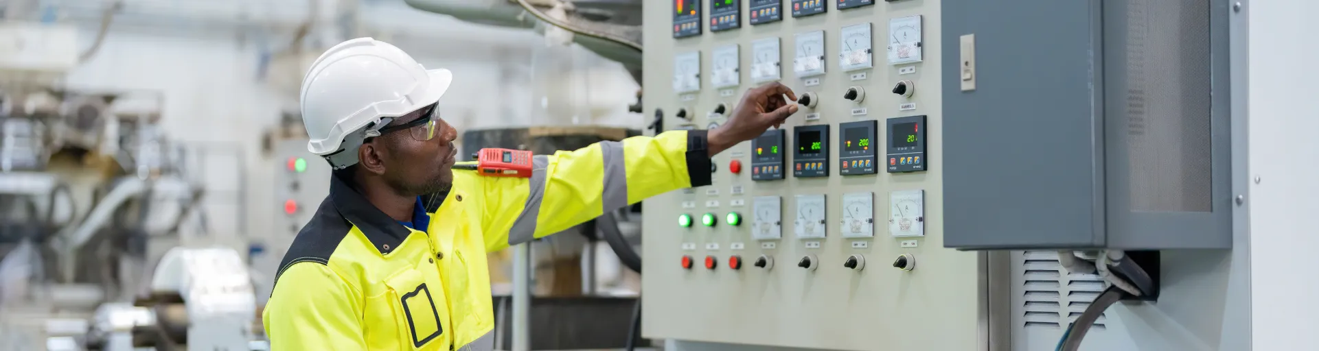 Engineer in a factory turning a knob, wearing reflective clothing and holding a clipboard